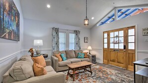 Ein Wohnzimmer mit einem beigen Sofa, einem Holztisch, gemusterten Vorhängen und einer Holztür.