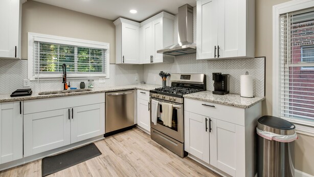A modern kitchen with white cabinets, stainless steel appliances, a built-in oven, and a window with blinds. - Modern Atlanta Vacation Rental Near Downtown! (Atlanta)