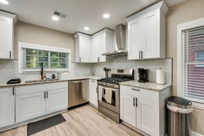 A modern kitchen with white cabinets, stainless steel appliances, a built-in oven, and a window with blinds. - Modern Atlanta Vacation Rental Near Downtown! (Atlanta)