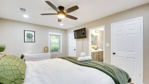A bedroom with a bed, a ceiling fan, a TV, a window, and a bathroom visible through an open door. - Modern Atlanta Vacation Rental Near Downtown! (Atlanta)
