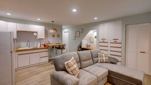 A modern kitchen with white cabinets, a dining area with a wooden table and chairs, and a living area with a grey sofa and pillows. - Cozy Rising Fawn Studio ~ 4 Mi to Cloudland Canyon (Rising Fawn)