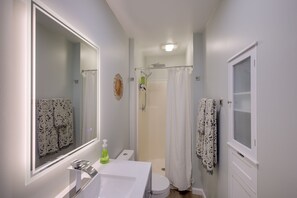 Une salle de bain avec un grand miroir, un lavabo blanc, des toilettes, une douche avec une porte en verre et un porte-serviettes.