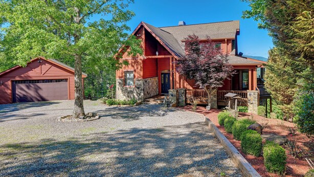 Eine zweistöckige Blockhütte mit Stein Fundament, einer Garage und einem gepflegten Vorgarten mit Kiesweg und angelegten Garten.