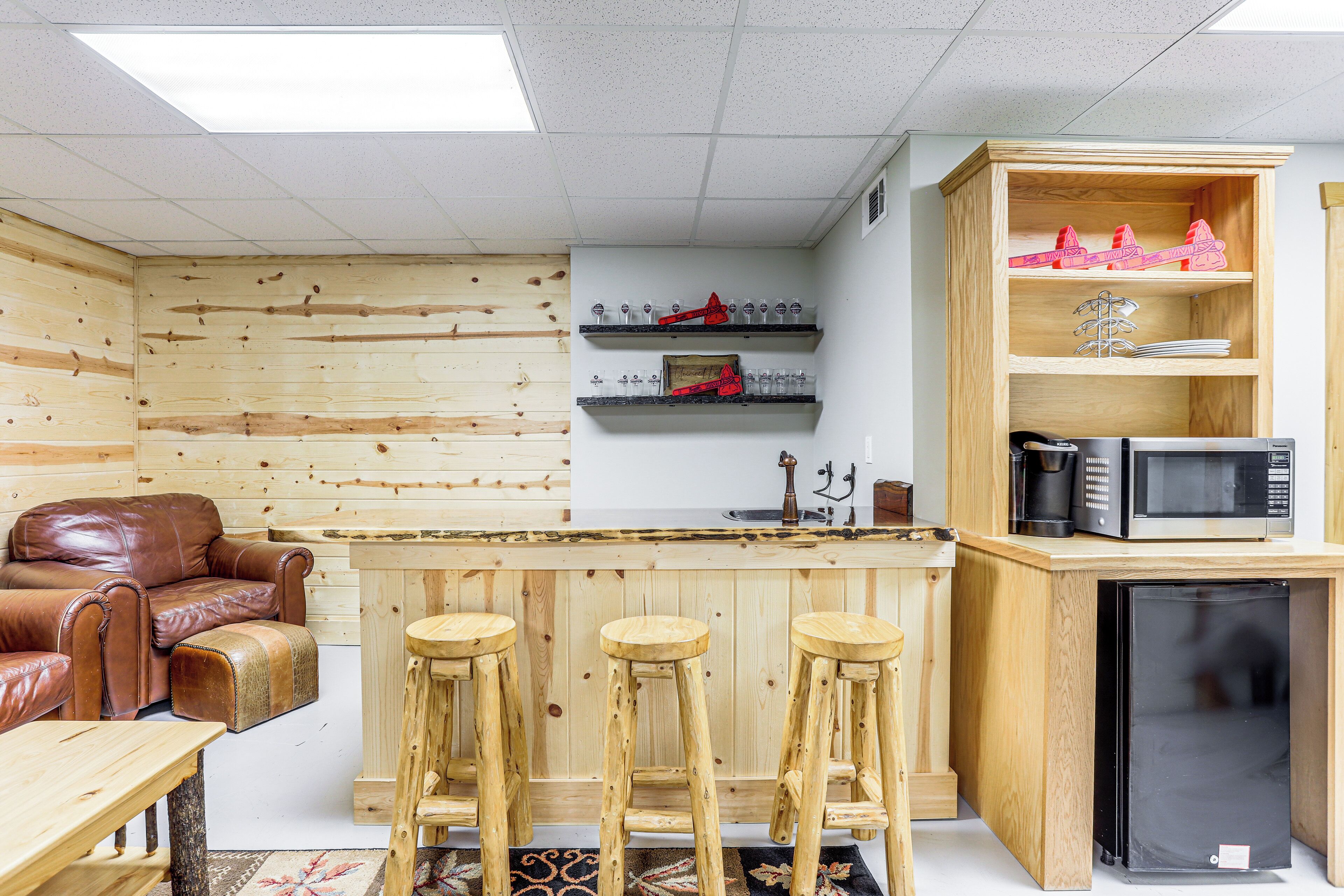 Een compacte keuken met houten barstoelen, een koelkast, een magnetron en planken met keukengerei.