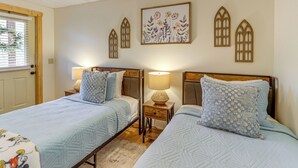A bedroom with two beds, wooden headboards, a nightstand with a lamp, and a floral wall art piece. - Game Room & Hot Tub: Upscale Ellijay Cabin! (Ellijay)