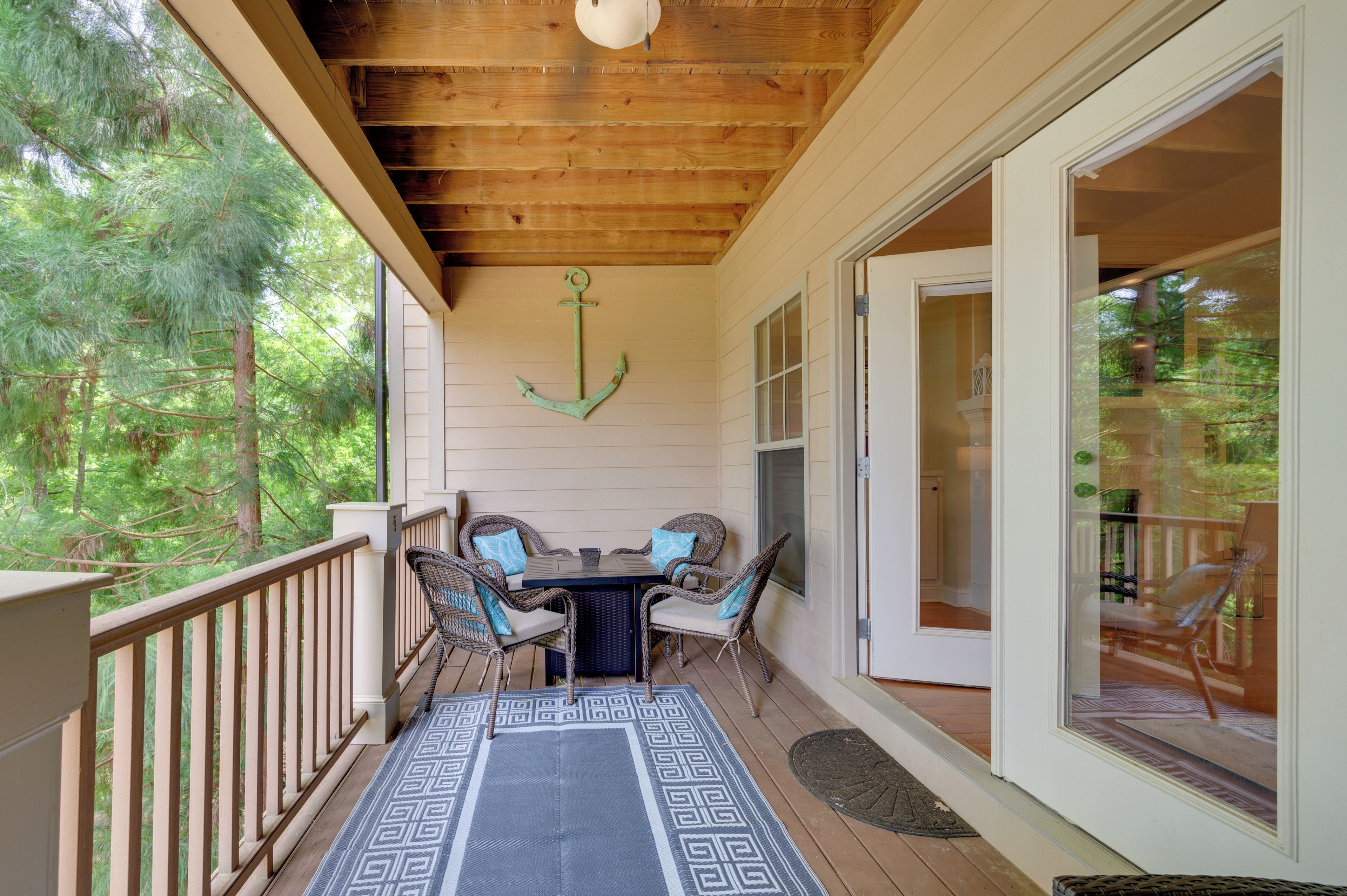 A covered porch with a table and chairs, a wooden ceiling, and a view of trees.