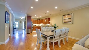A spacious dining area with a wooden table and white chairs, a kitchen in the background, and a framed picture on the wall. - Lake Oconee Abode w/ Patio, Grill & Fire Pit Table (Eatonton)