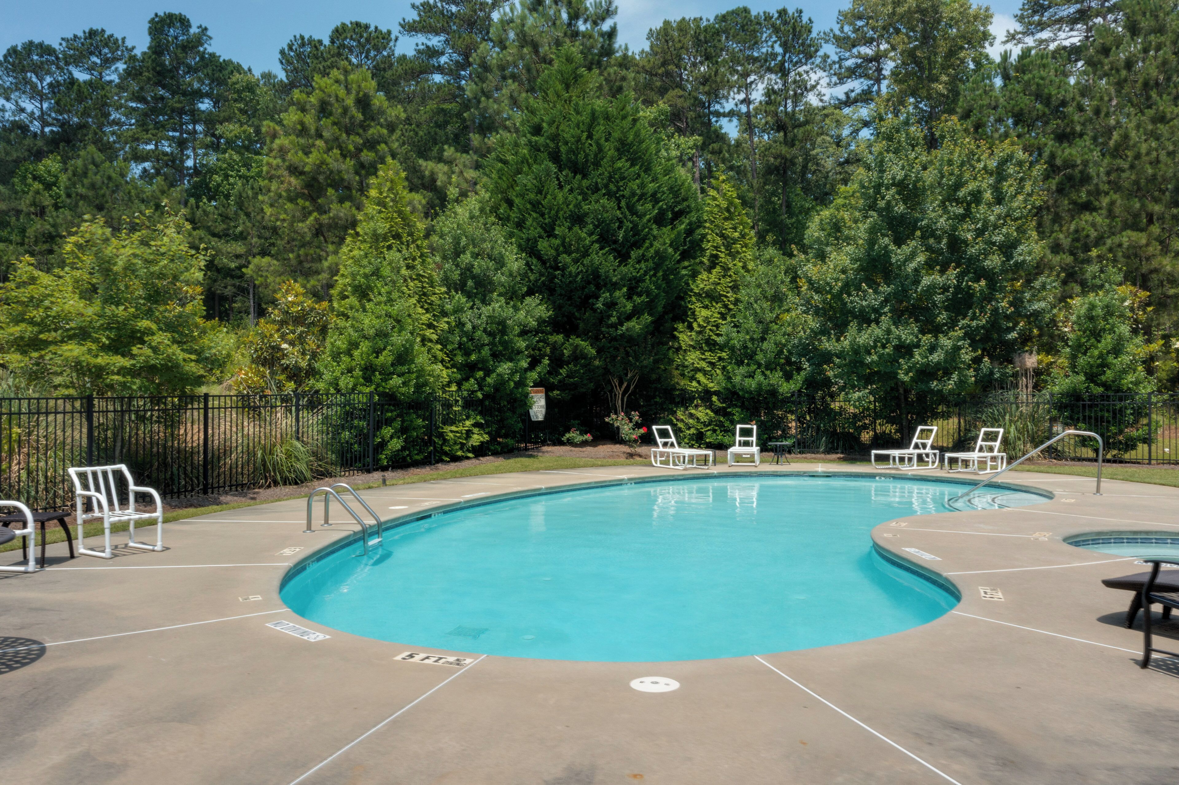 A swimming pool with a surrounding deck, lounge chairs, and a fence.