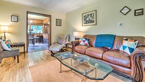 A living room with a brown leather sofa, glass coffee table, and a dining area with a wooden table and chairs.