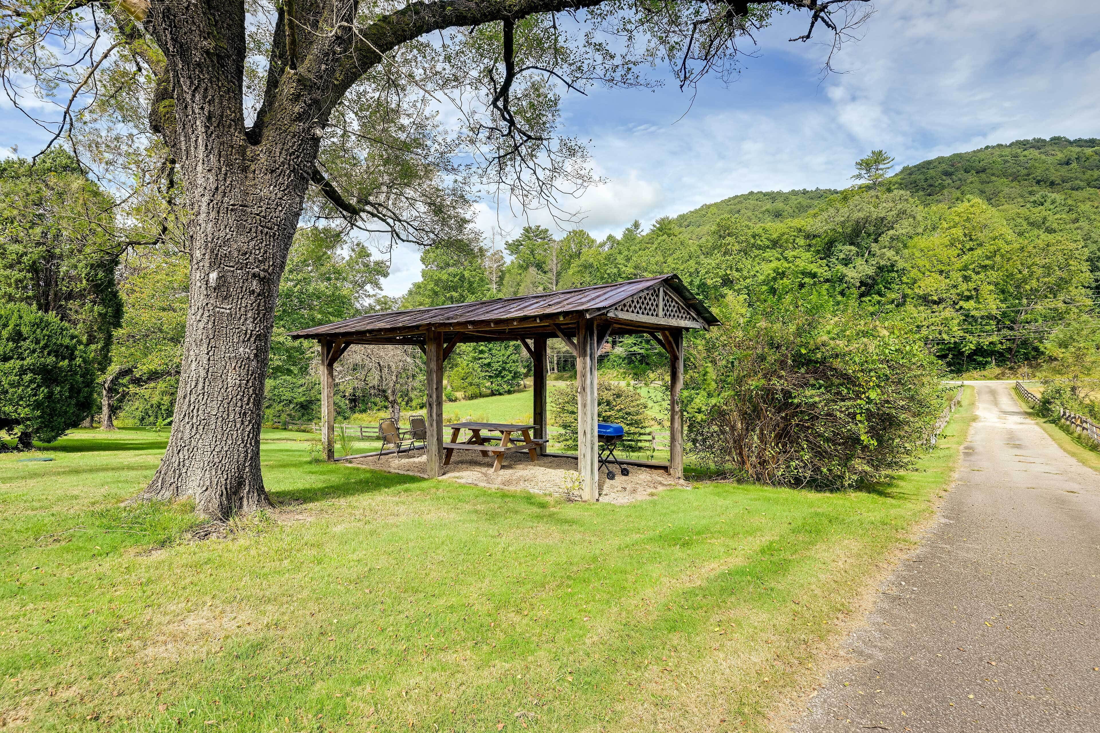 A wooden gazebo with benches and a picnic table in a grassy area.