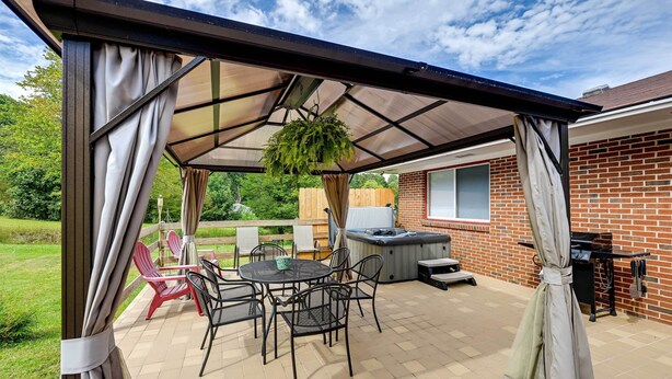 An outdoor patio with a covered seating area, a hot tub, and a brick wall.