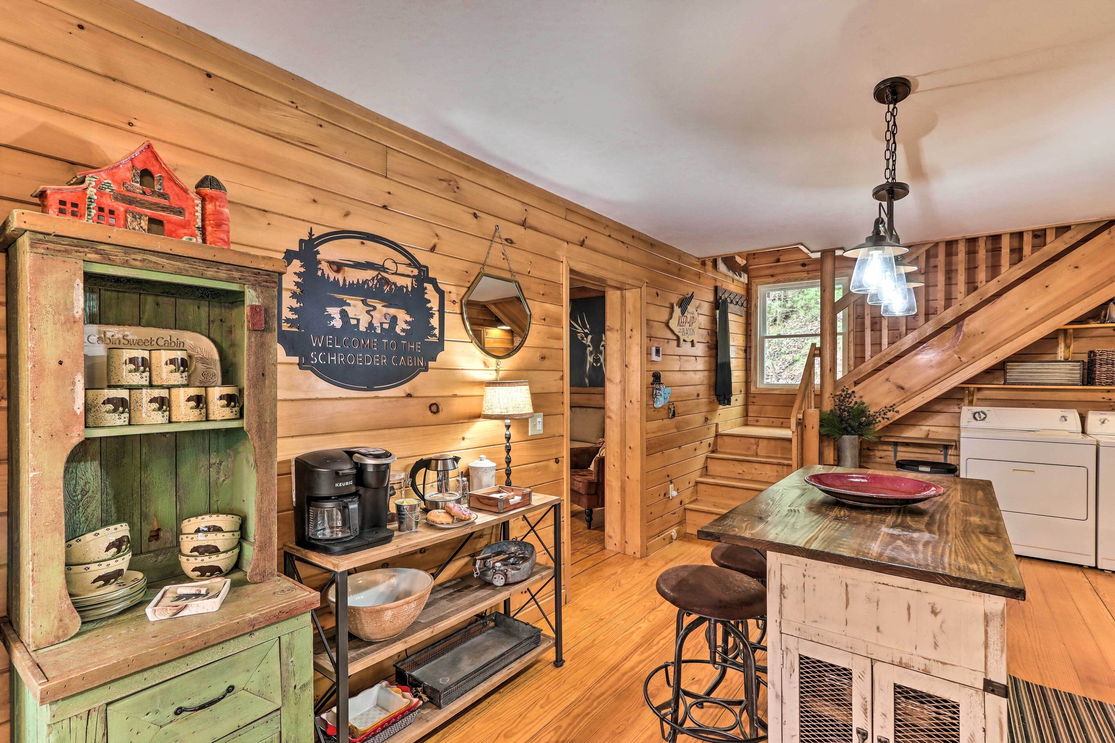 A cozy cabin interior with a wooden interior, a kitchen area with a coffee maker, and a sign welcoming guests to the cabin.