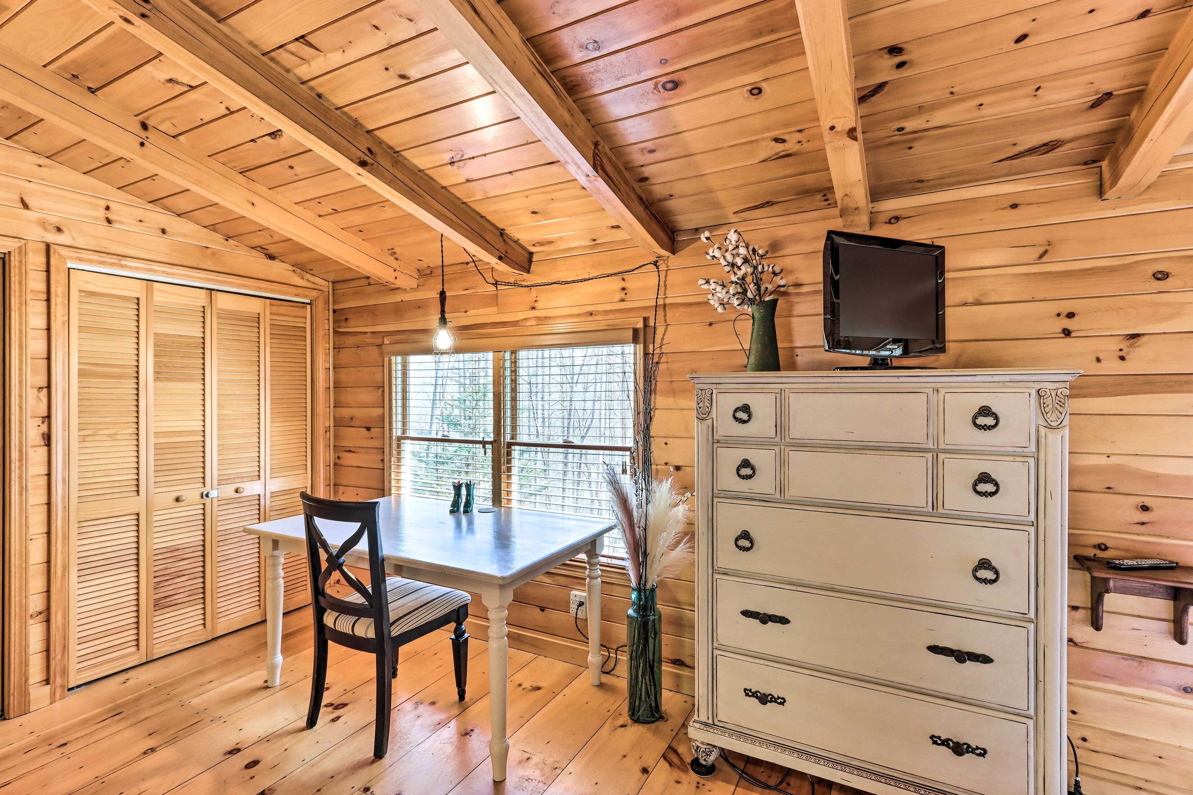 A wooden interior with a dining table, chairs, a dresser, and a television on the wall.
