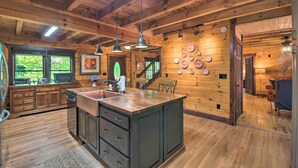 A wooden cabin interior with a kitchen area featuring a large island, wooden cabinets, and a dining area with a staircase. - Rural Dallas Gem w/ Hot Tub, Sauna + Fire Pit! (Dallas)