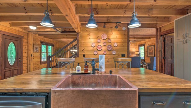 A wooden cabin interior with a large kitchen area, wooden ceiling beams, and a dining table with chairs. - Rural Dallas Gem w/ Hot Tub, Sauna + Fire Pit! (Dallas)