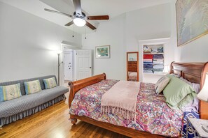 A bedroom with a wooden bed, a gray sofa, a ceiling fan, and a white door. - Hampton Sanctuary w/ Fire Pit & Fenced Yard! (Hampton)