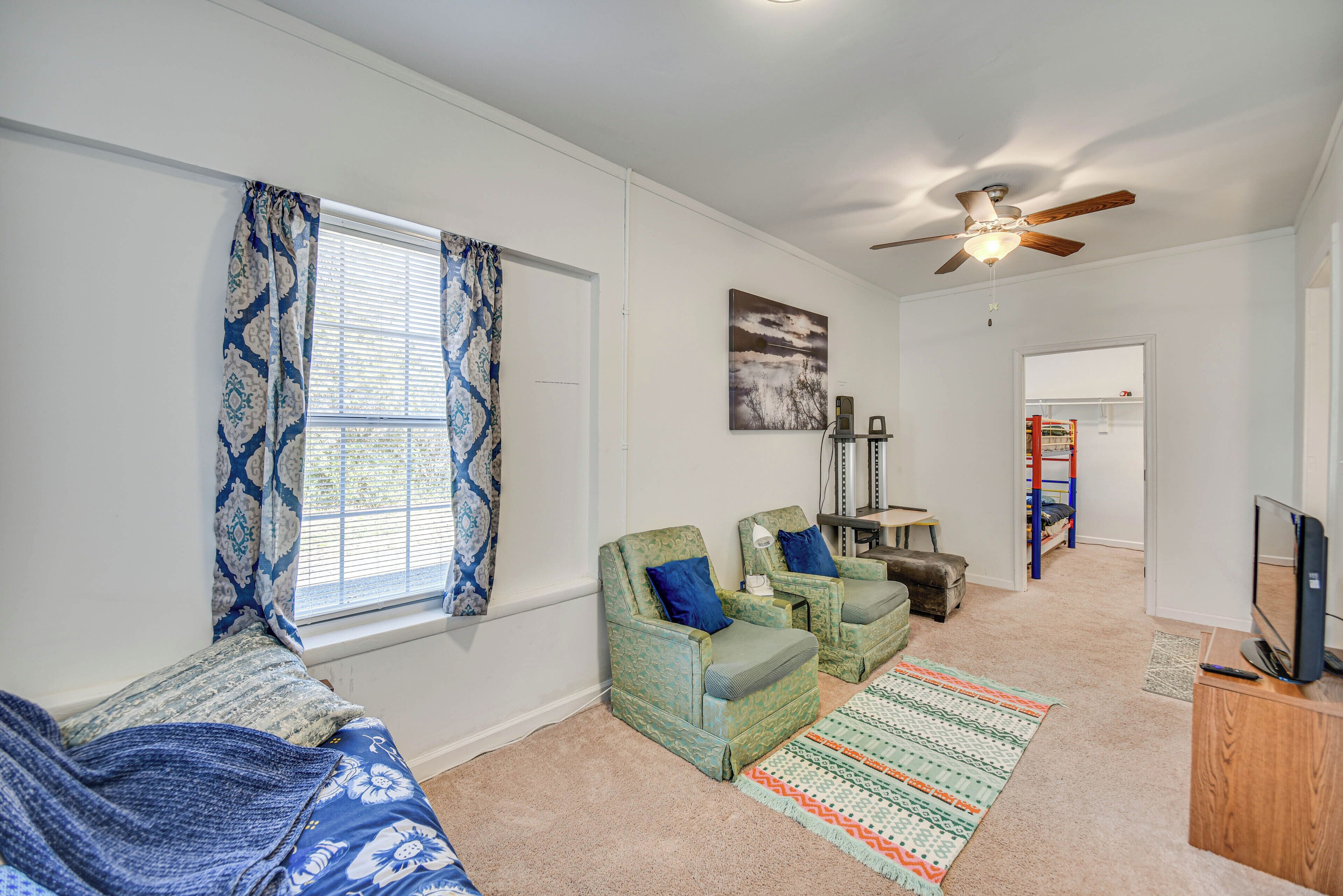 A living room with two green armchairs, a sofa, a ceiling fan, a TV, and a window with patterned curtains.