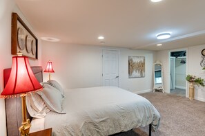 A bedroom with a bed, two bedside lamps, a door, a painting, and a closet.