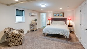 A bedroom with a bed, a patterned armchair, a small table with decorative items, and two bedside lamps.