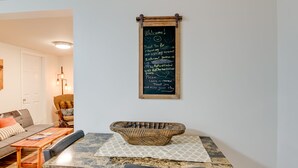 A dining area with a wooden table, a black chair, and a woven basket on the table. A chalkboard sign with a message is mounted on the wall above the table.