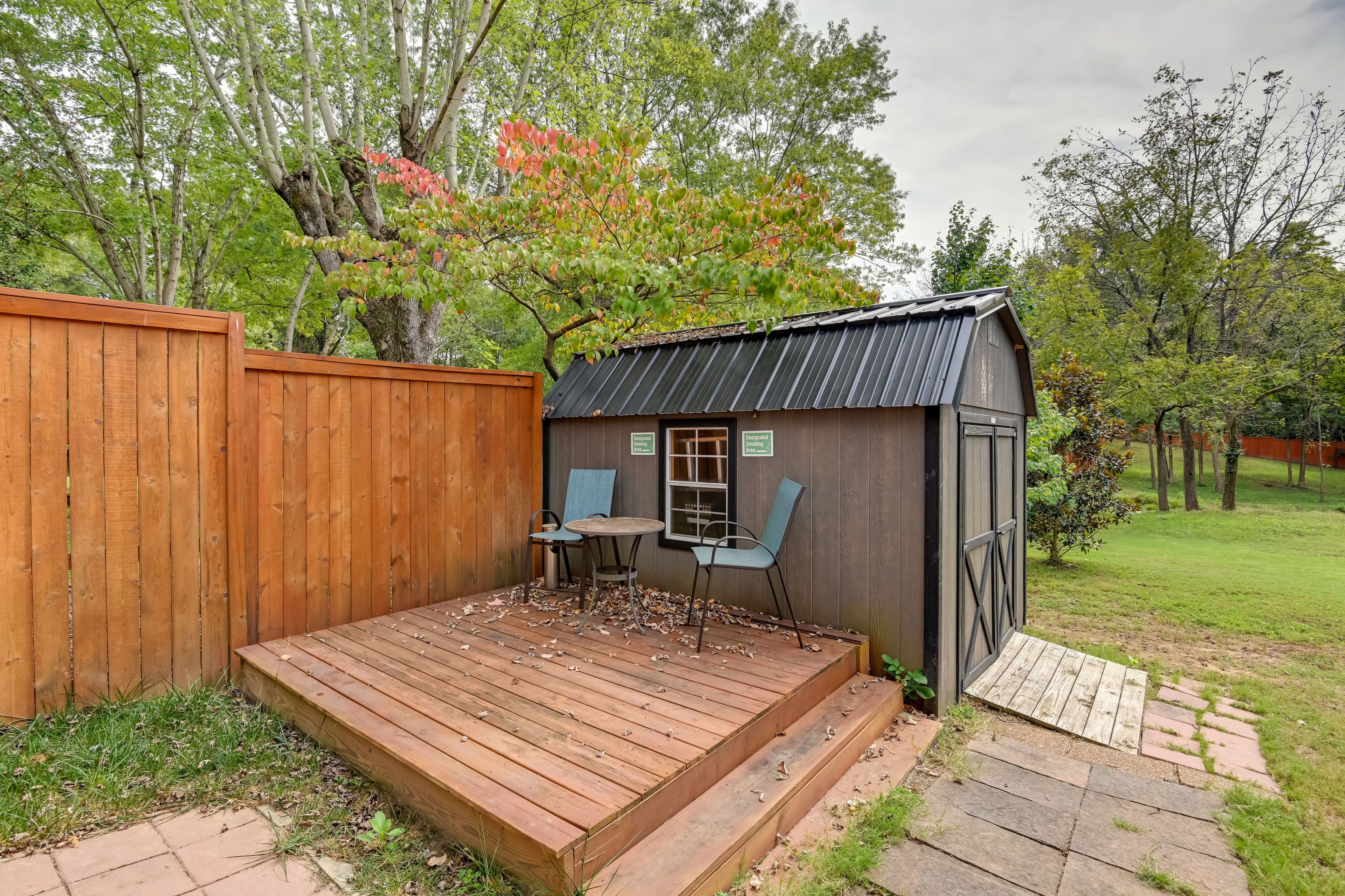 Une terrasse en bois avec une table et des chaises, un abri de jardin avec un toit en métal et une clôture en bois.
