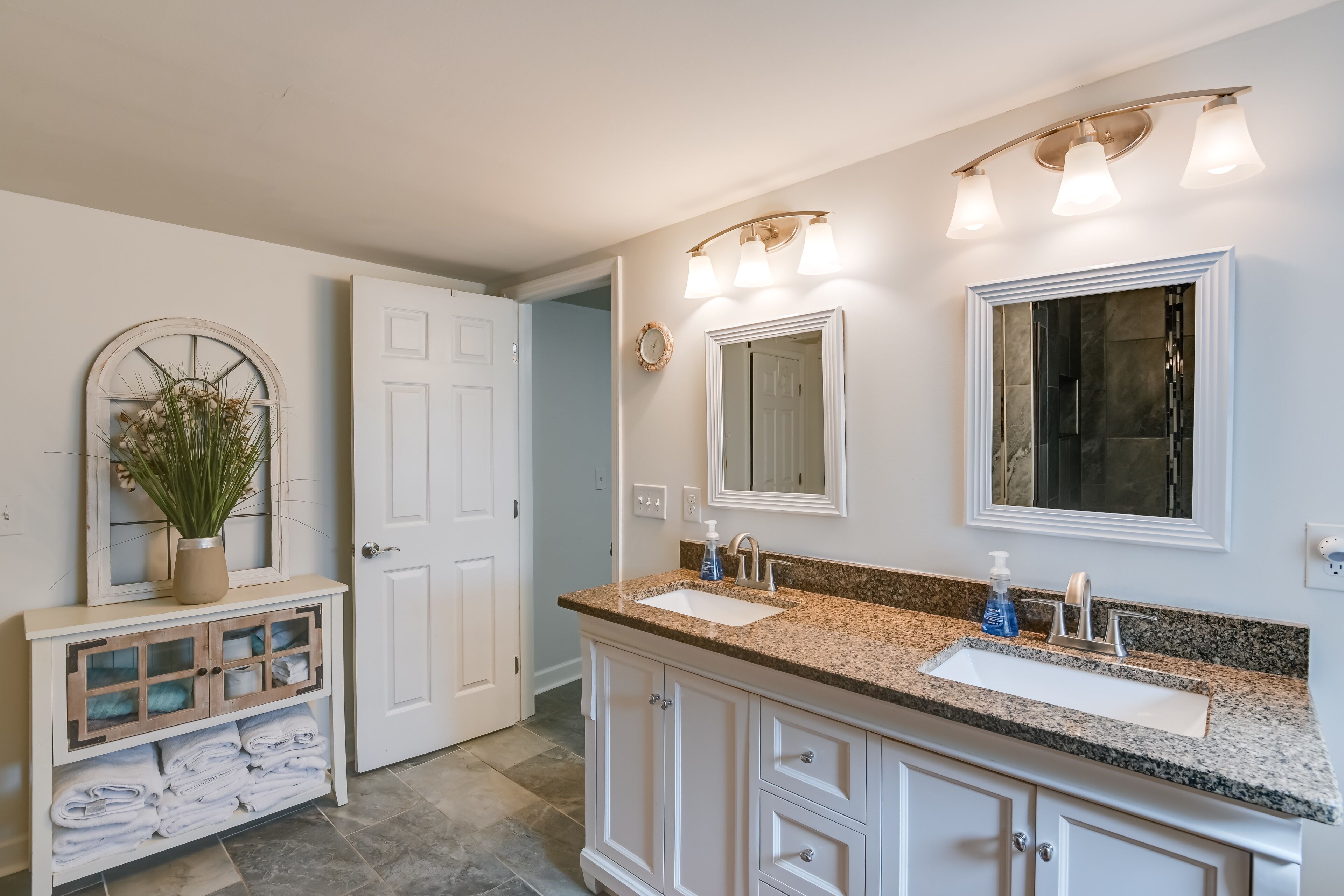 A bathroom with a double sink vanity, a mirror, a towel rack, and a door.