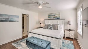 Une chambre à coucher avec un lit blanc, un ventilateur de plafond, une table de chevet avec une lampe et une fenêtre avec des stores.