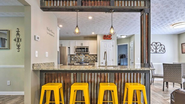 A kitchen with a bar area, featuring a central island with stools, a refrigerator, and a microwave. - Charming Covington Home w/ Fire Pit + Game Room! (Covington)