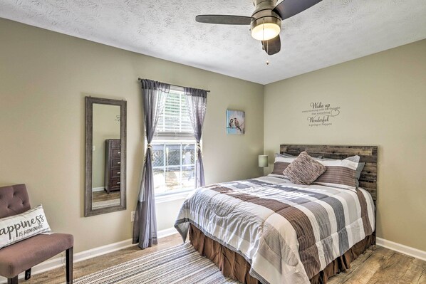 Une chambre à coucher comprenant un lit, une chaise, un miroir, une fenêtre avec des rideaux, un ventilateur de plafond et une citation inspirante sur le mur.