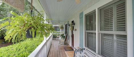 A wooden porch with a ceiling fan, white railings, and a bench.