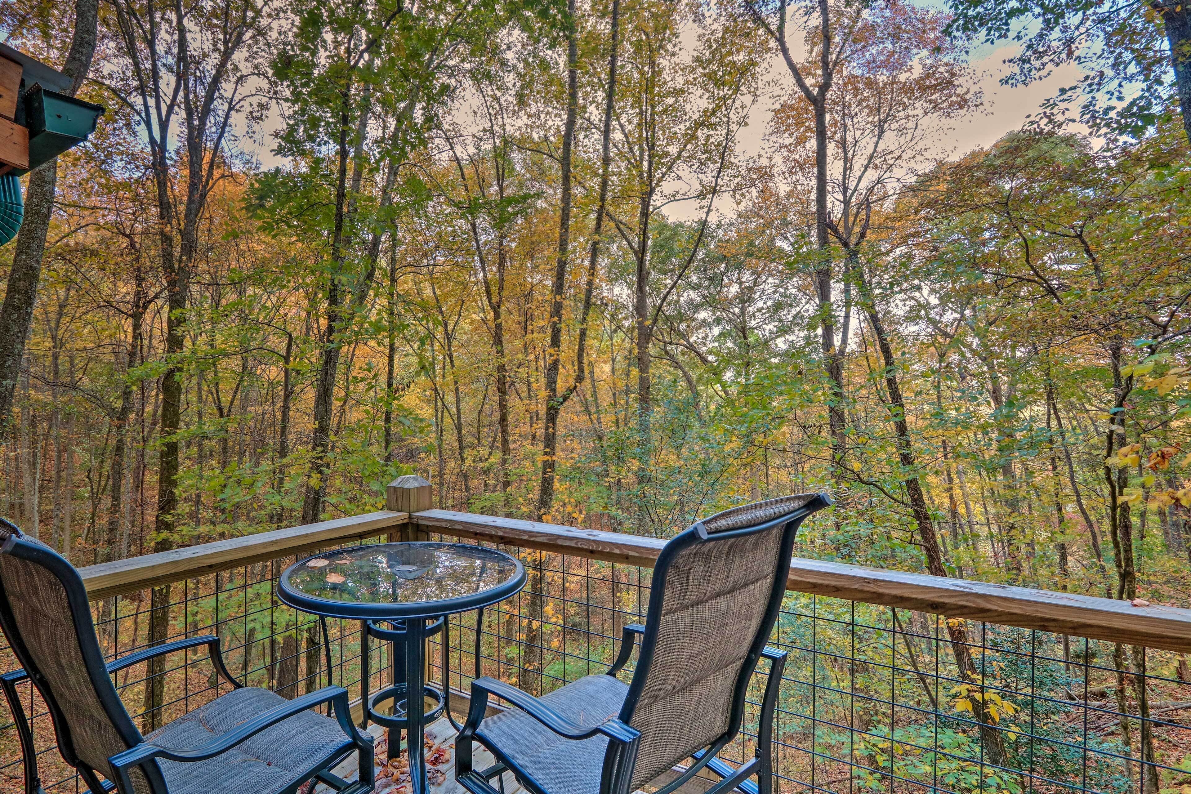 A balcony with a table and chairs overlooking a forested area.