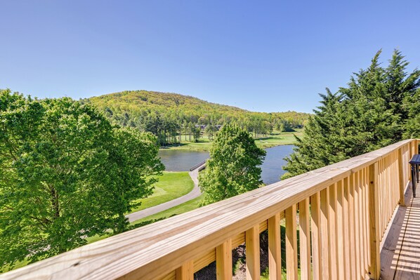 A wooden deck overlooking a lake with a forested hill in the background. - Charming Condo on Sky Valley Golf Course! (Dillard)