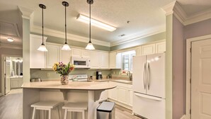 A kitchen with white cabinets, a central island with stools, a trash bin, and pendant lighting. - Sunny Clayton Condo on Kingwood Golf Course! (Clayton)