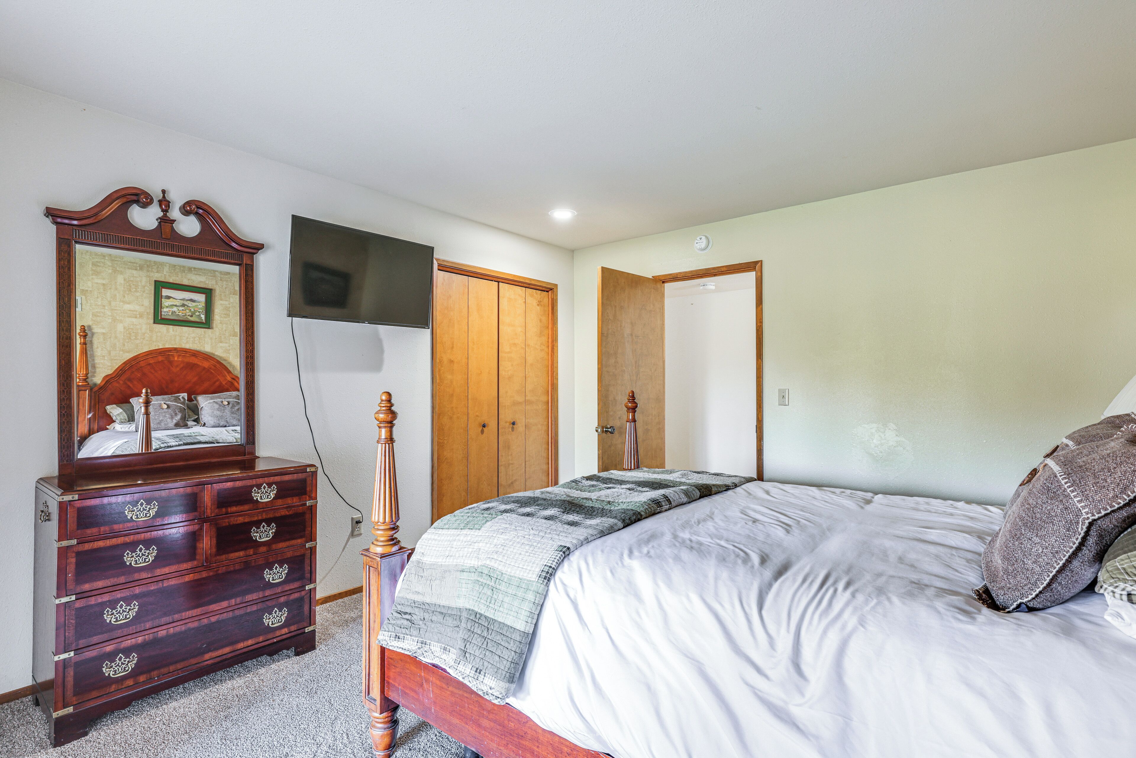A bedroom with a wooden dresser, a bed with a quilt, and a television mounted on the wall.