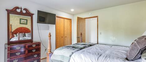 A bedroom with a wooden dresser, a bed with a quilt, and a television mounted on the wall.