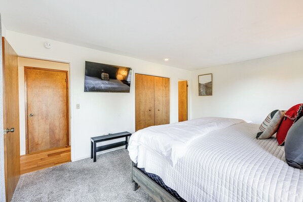 A bedroom with a large bed, wooden doors, a bench, and a wall-mounted TV. - Groveland Home w/ Deck: 2 Mi to Pine Mountain Lake (Groveland)