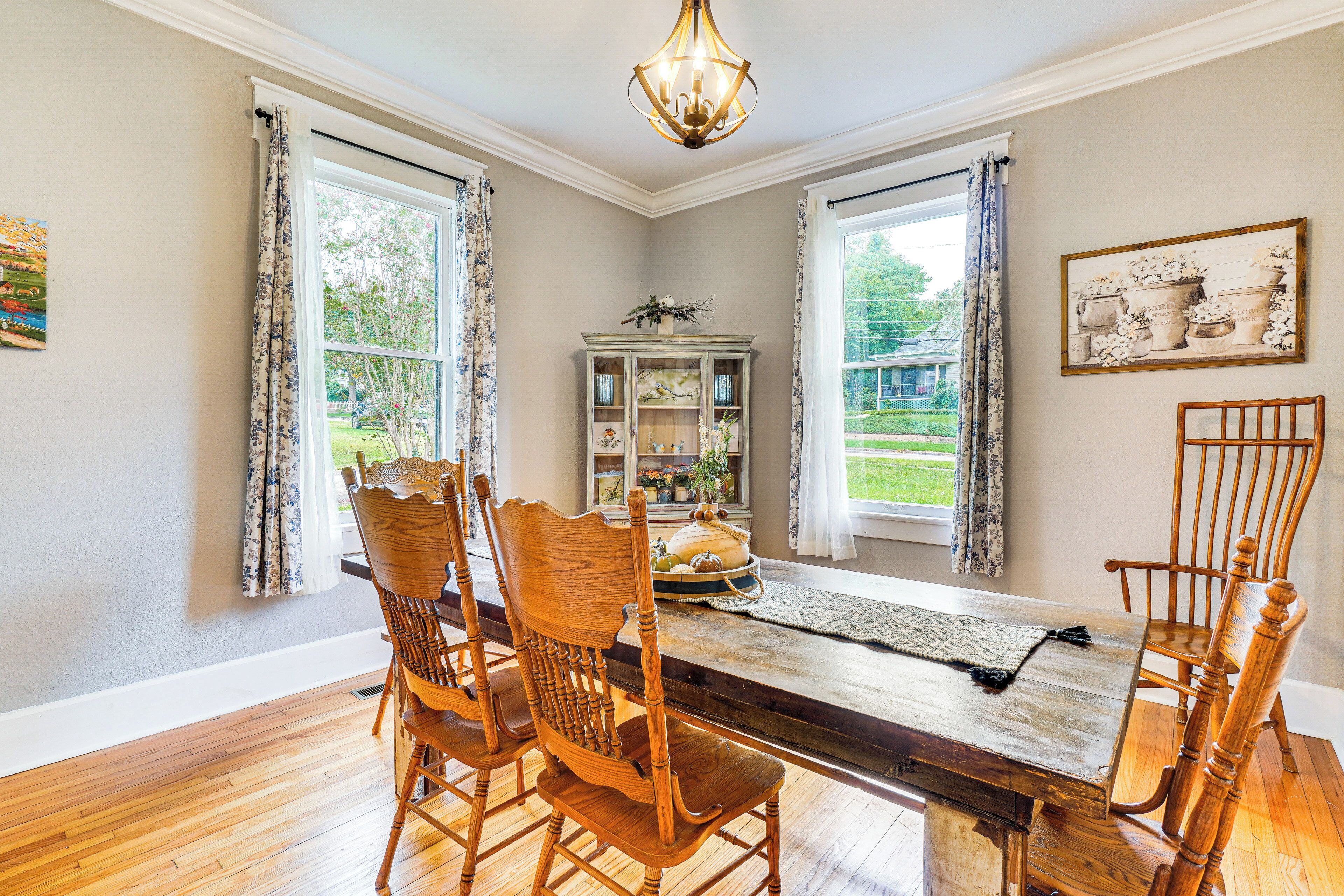 Une salle à manger avec une table et des chaises en bois, un lustre et une vue sur l’extérieur grâce à de grandes fenêtres.