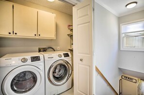 Uma lavanderia com duas máquinas de lavar Samsung brancas, uma porta e uma pequena prateleira com uma caixa rotulada "HOVIE".