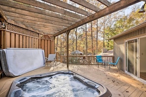 Um deck de madeira com hidromassagem, área de estar externa e um espaço coberto com pérgola.