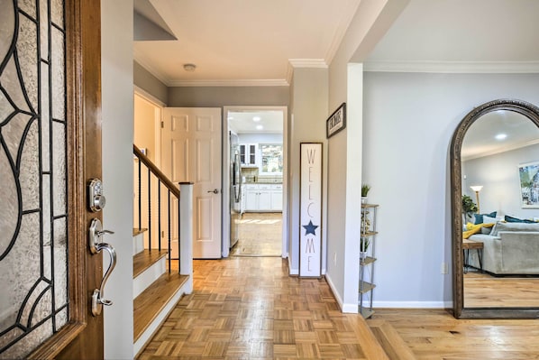 Um corredor com piso de madeira, porta de vidro com moldura de metal, escada e vista para uma cozinha.