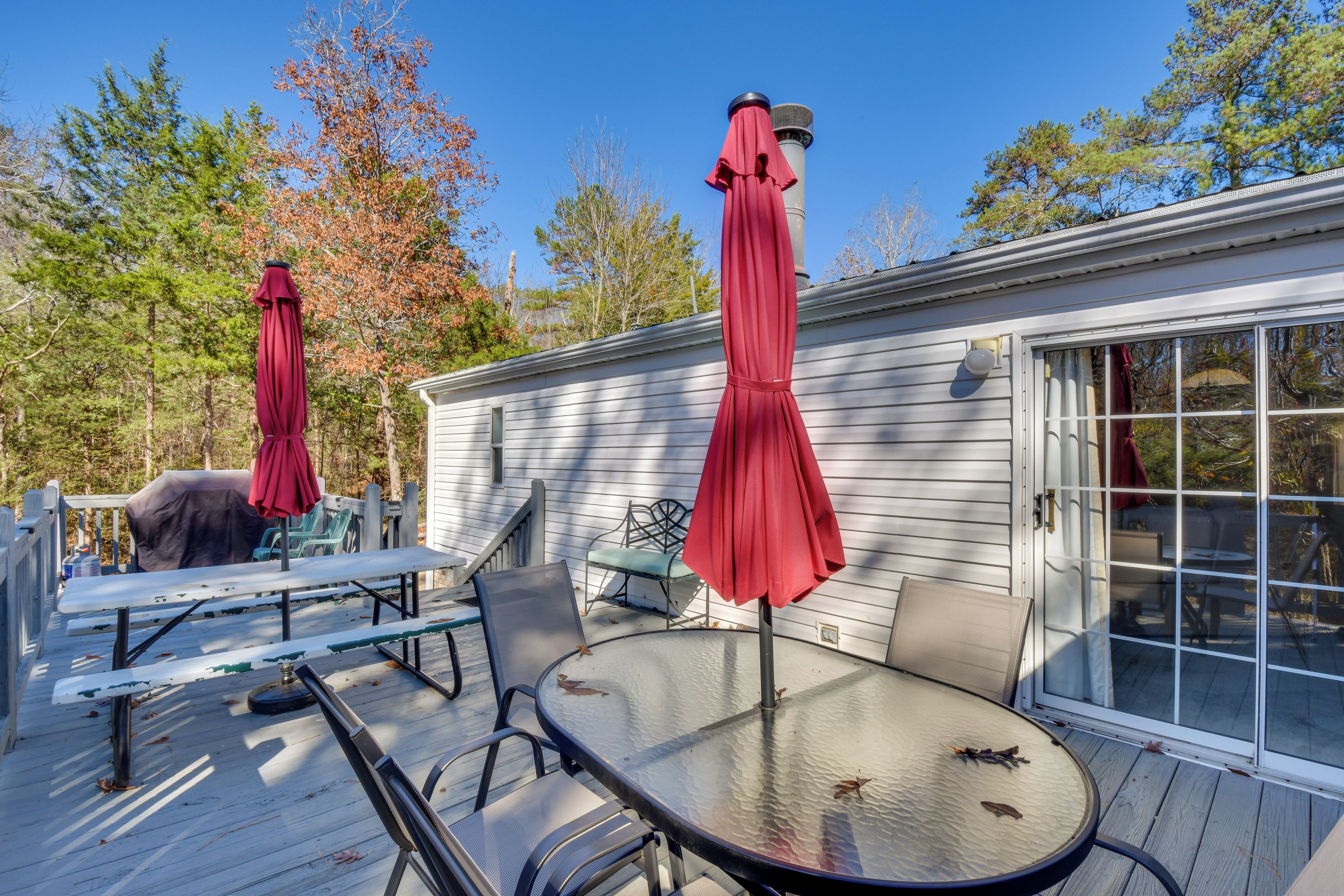A deck with a round glass table and chairs, red umbrellas, and a covered grill.