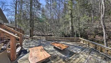 A wooden deck with picnic tables, surrounded by a forested area.