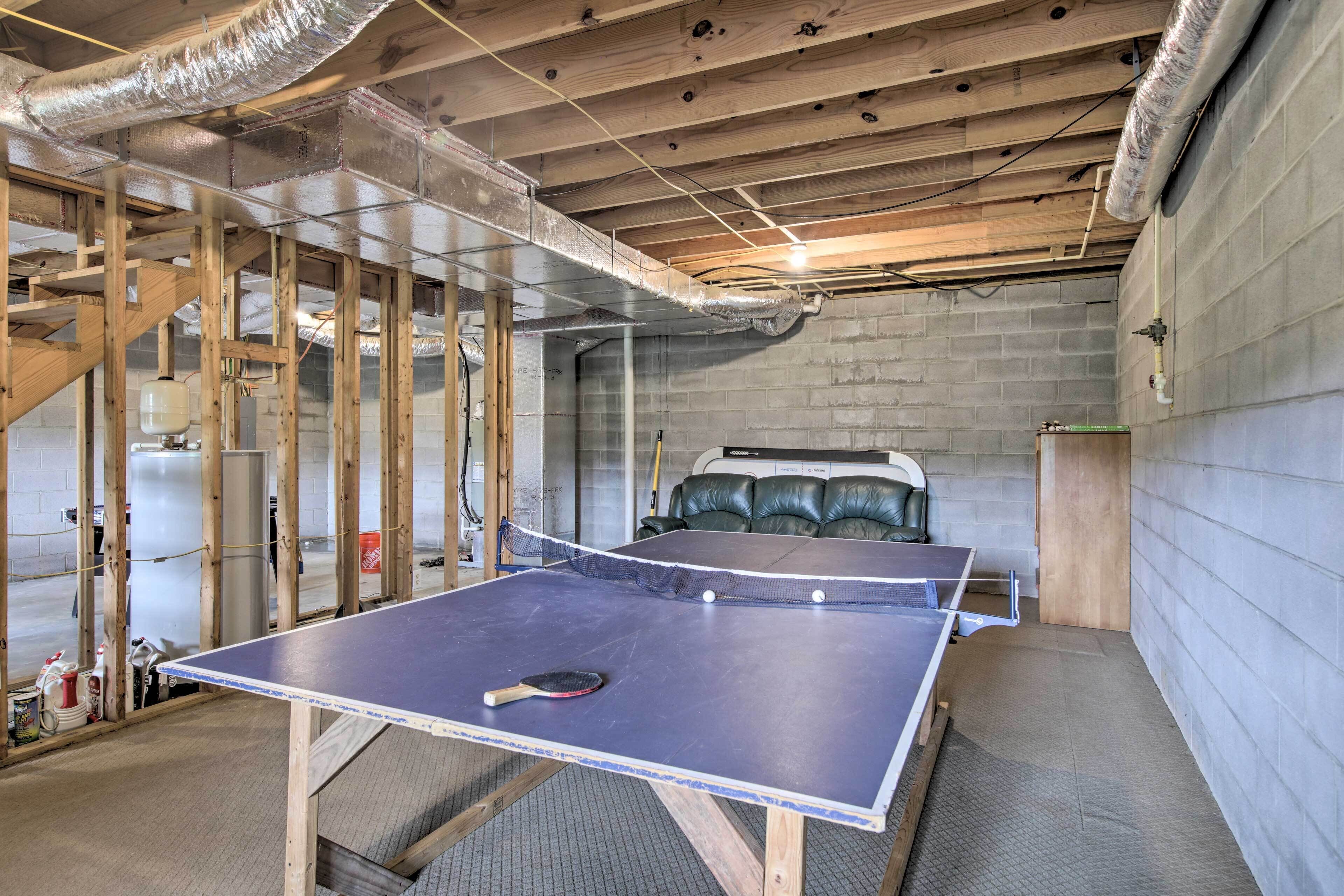A room with a ping pong table, a bed, and a concrete wall.