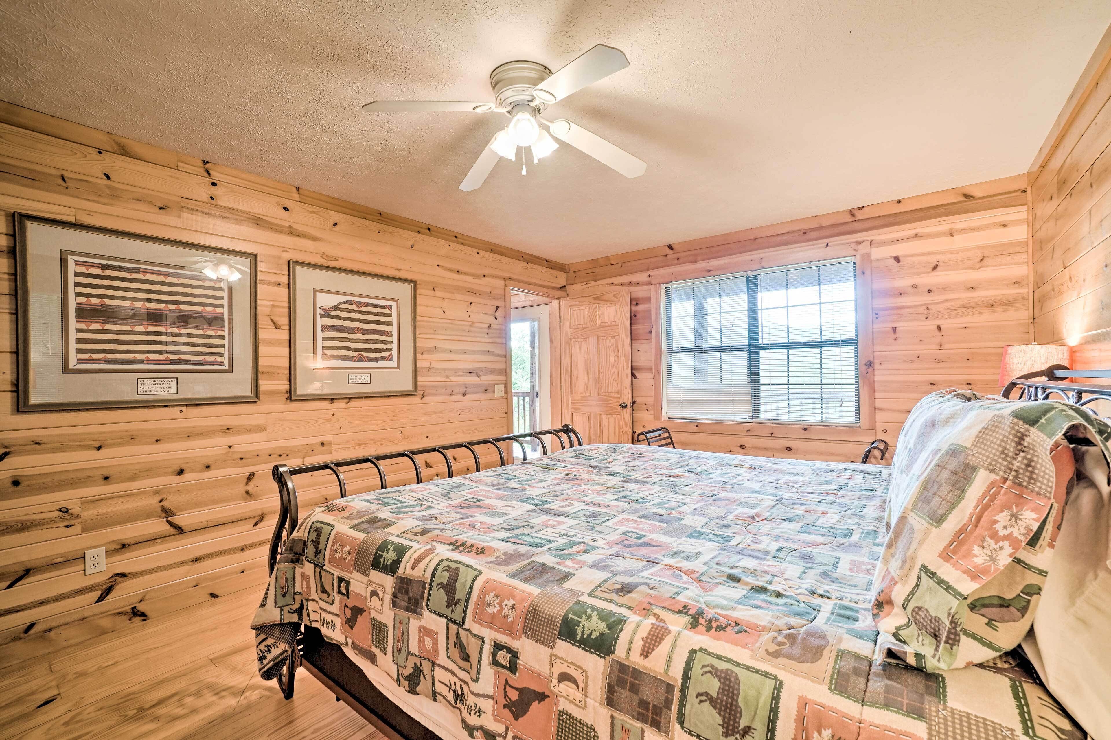 A wooden-paneled bedroom with a bed, ceiling fan, framed pictures, and a window.