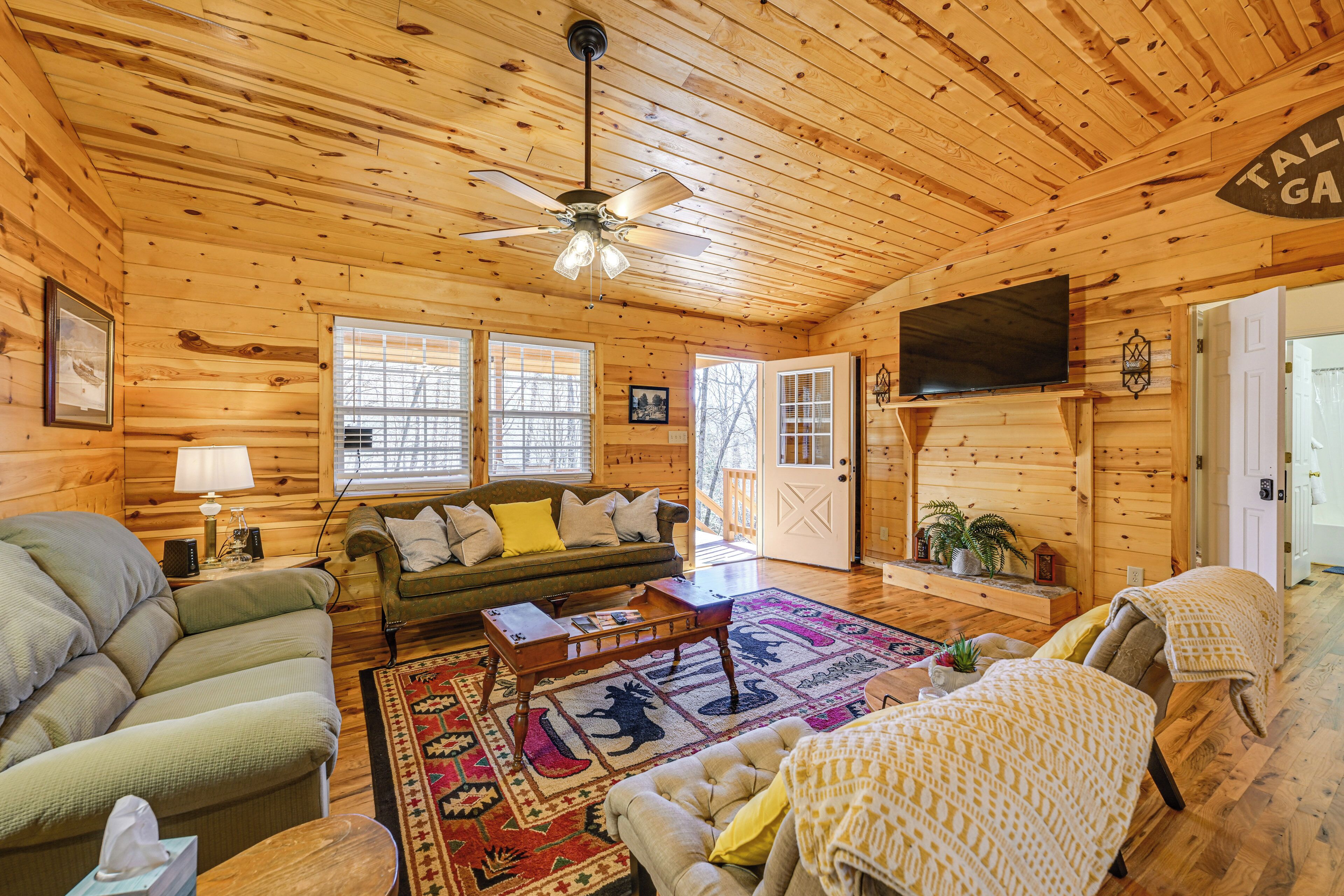 L’intérieur d’un chalet confortable, avec un salon, un canapé, une table basse, un téléviseur et une porte donnant sur l’extérieur.