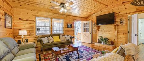 L’intérieur d’un chalet confortable, avec un salon, un canapé, une table basse, un téléviseur et une porte donnant sur l’extérieur.
