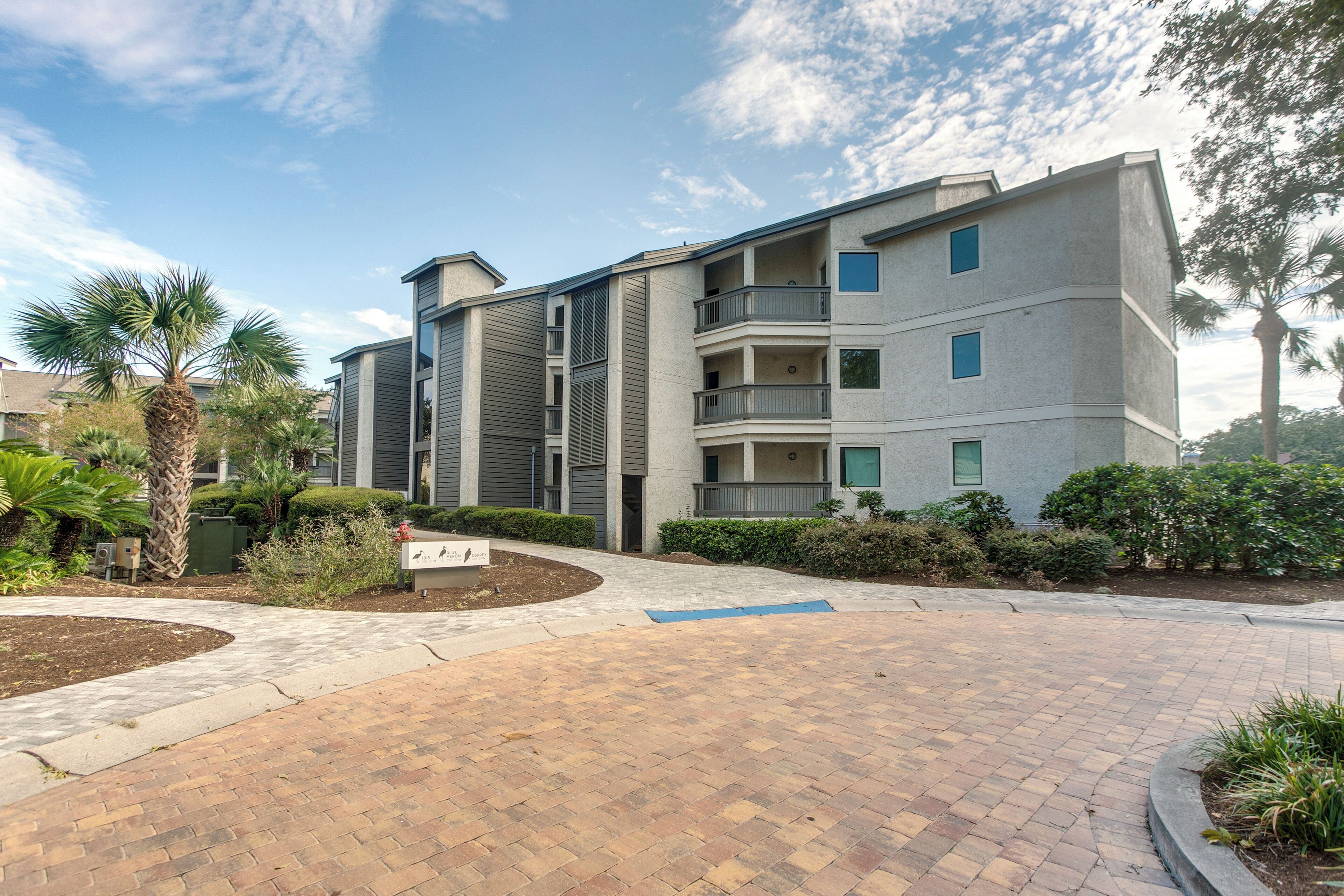 A multi-story residential building with balconies, a landscaped garden, and a paved entrance area.
