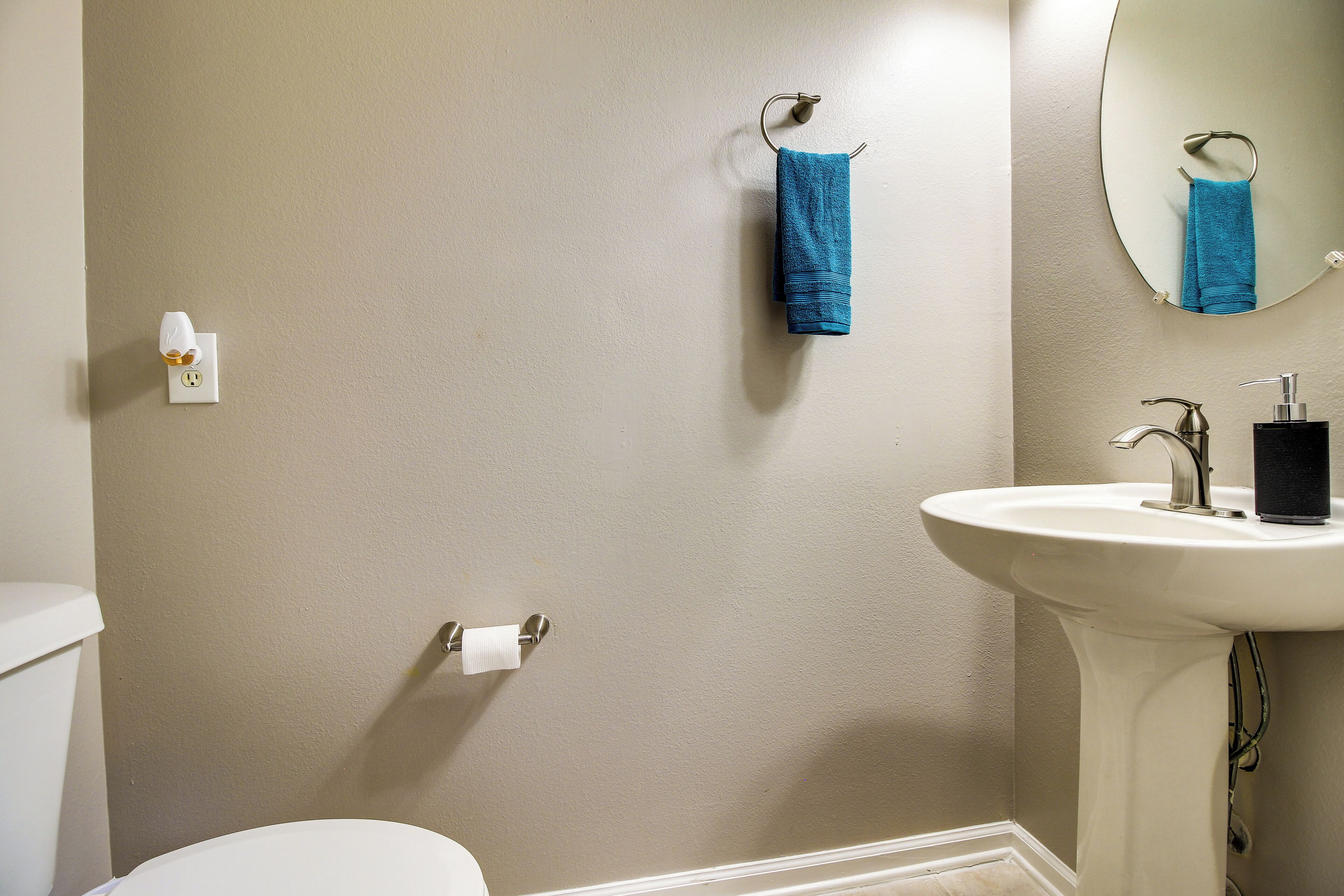 Ein Badezimmer mit weißem Waschbecken, einem Spiegel, einem Handtuchhalter mit blauem Handtuch, einer Toilette und einer wandmontierten Leuchte.