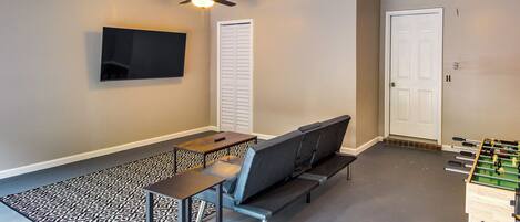 A room with a sofa, a foosball table, a TV, and a patterned rug.