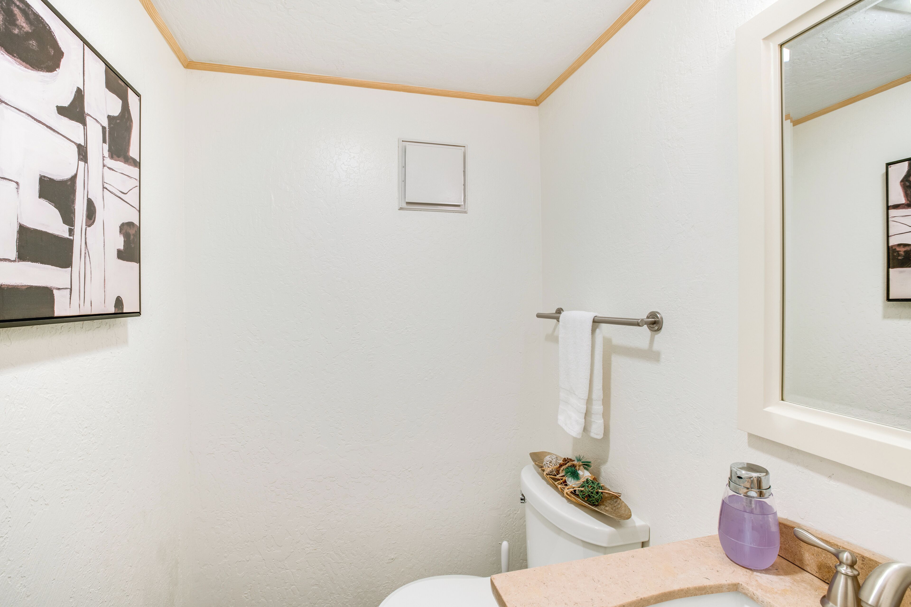 A bathroom with a white toilet, a sink with a beige countertop, a towel rack, and a small window.